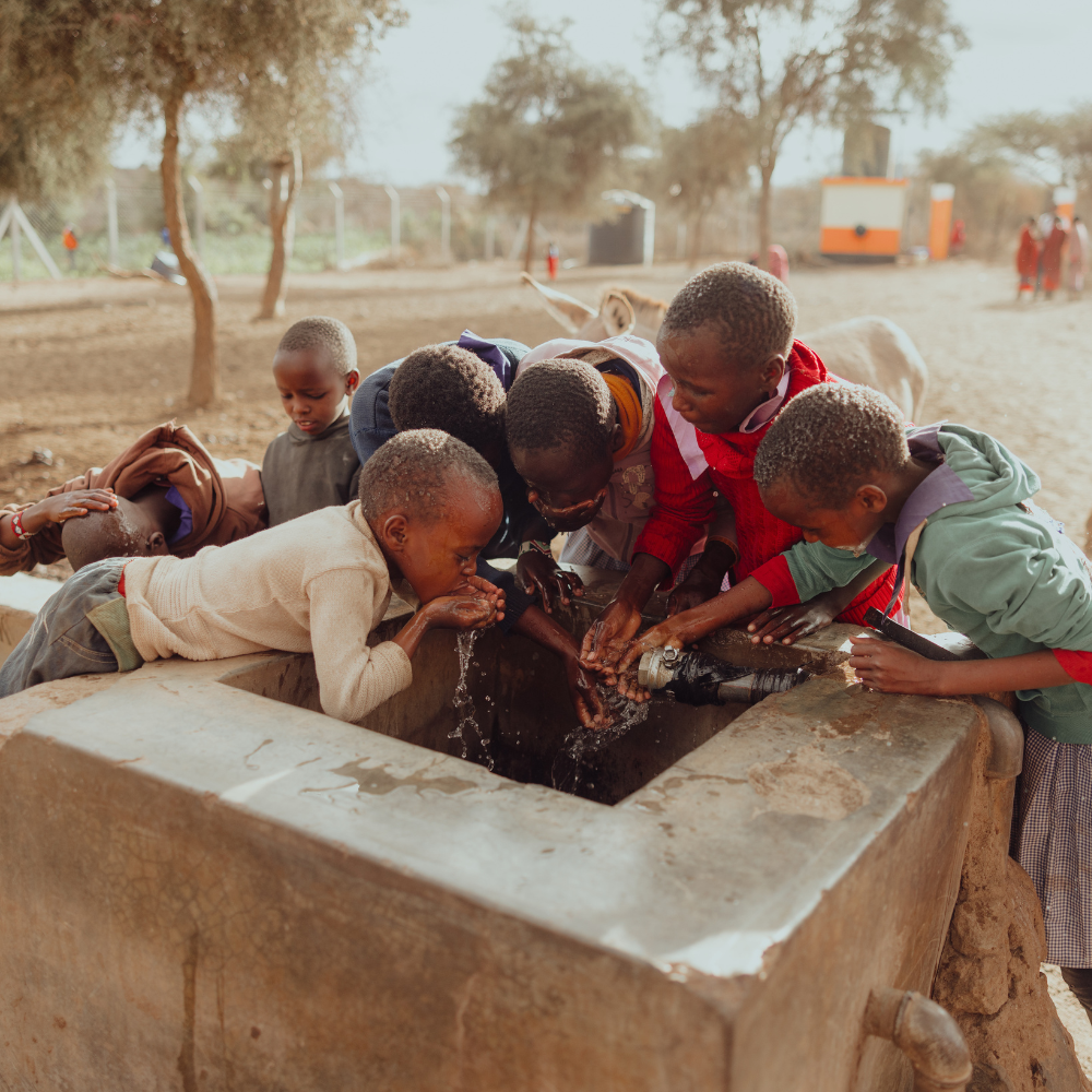 Kinderen rondom een waterput, ze drinken.